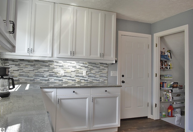 kitchen with white cabinets, backsplash, stone countertops, and dark wood-type flooring