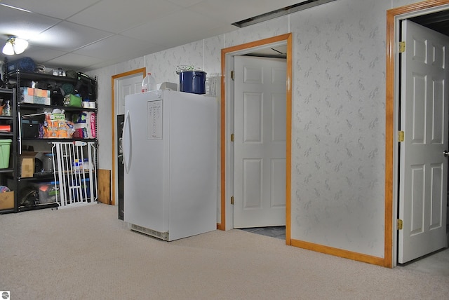 basement with a paneled ceiling, freestanding refrigerator, and carpet