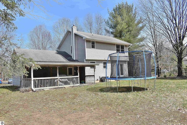 back of house with a yard, a trampoline, a porch, and a chimney