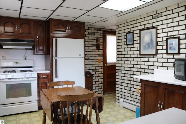 kitchen with under cabinet range hood, light floors, light countertops, white appliances, and brick wall