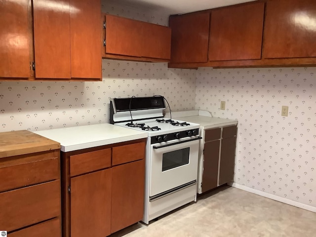 kitchen with baseboards, light countertops, wallpapered walls, and gas range gas stove