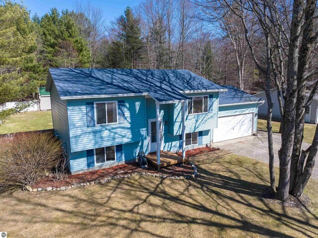 1294 Fisher Rd, Traverse City, MI 49685 - bi-level home featuring a forest view, a front lawn, roof with shingles, and a detached garage