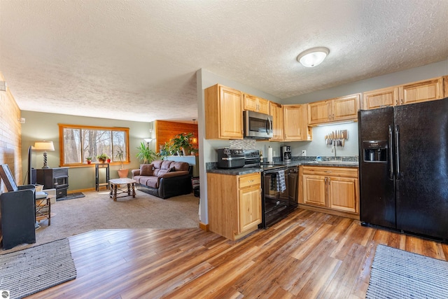 1294 Fisher Rd, Traverse City, MI 49685 - kitchen featuring dark countertops, a wood stove, black appliances, a textured ceiling, and open floor plan