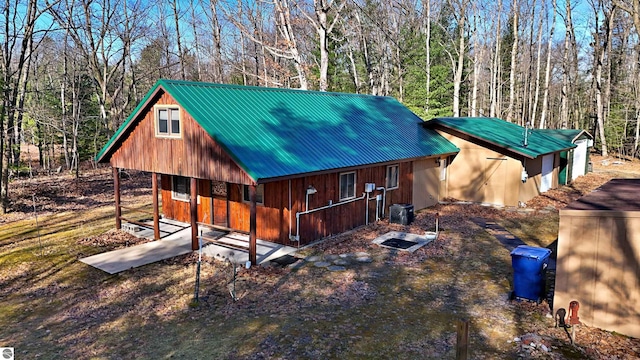 8991 W Oak Ln, Lake City, MI 49651 - view of front of house featuring metal roof, central AC unit, a forest view, and a porch