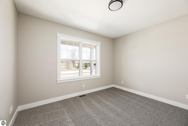 empty room featuring dark colored carpet, visible vents, and baseboards