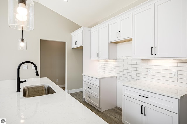 kitchen with wood finished floors, a sink, backsplash, and light stone counters