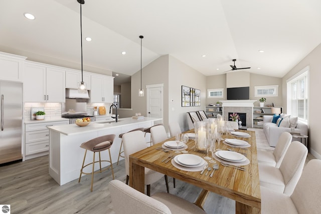 dining room featuring vaulted ceiling, recessed lighting, light wood-style floors, ceiling fan, and a fireplace