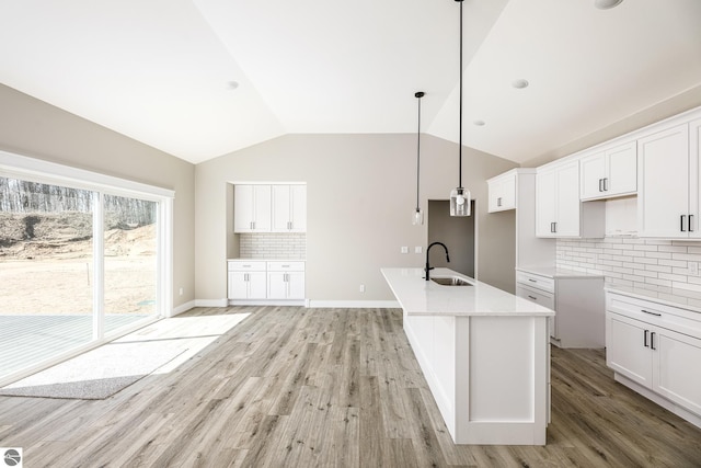 kitchen featuring vaulted ceiling, tasteful backsplash, a sink, a center island with sink, and light wood finished floors