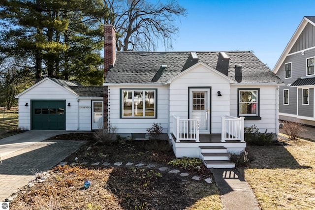 view of front of home featuring a chimney, an attached garage, driveway, and roof with shingles