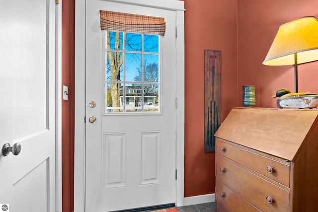 doorway to outside with baseboards and dark tile patterned flooring