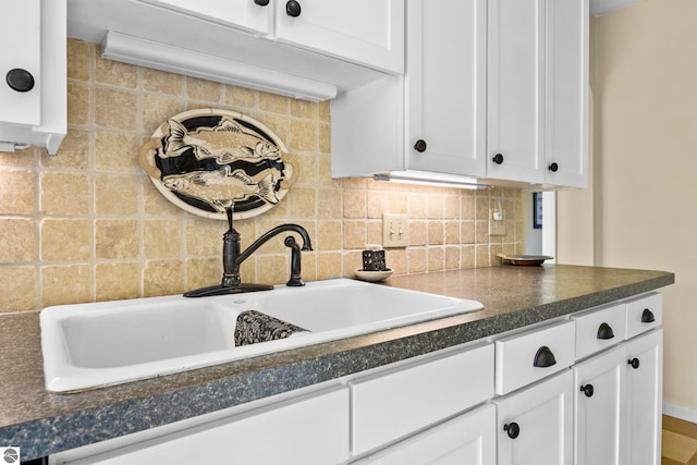 kitchen featuring decorative backsplash, dark countertops, a sink, and white cabinets