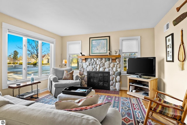 living area with visible vents, baseboards, a stone fireplace, and wood finished floors