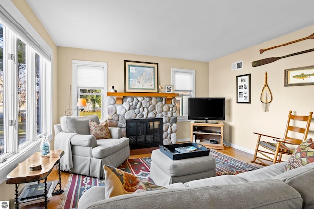 living room with a stone fireplace, wood finished floors, visible vents, and baseboards