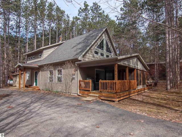 view of side of property with aphalt driveway, covered porch, and roof with shingles