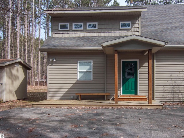 view of front facade with a shingled roof, a storage unit, and an outdoor structure