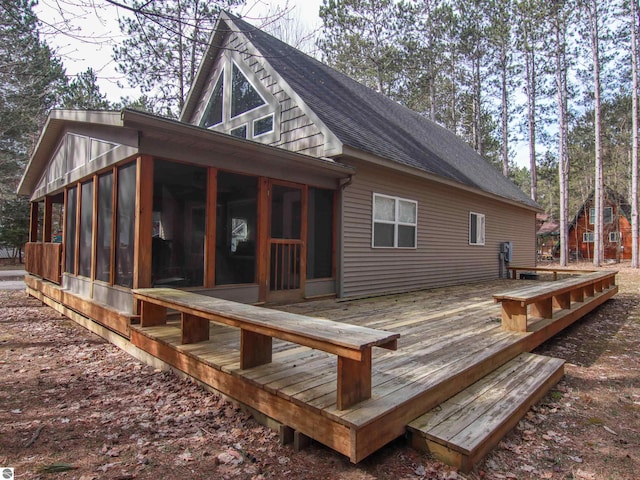 back of property with a wooden deck, a sunroom, and roof with shingles