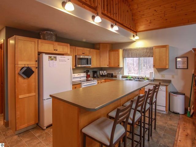 kitchen featuring a center island, a sink, a kitchen bar, white appliances, and light brown cabinets