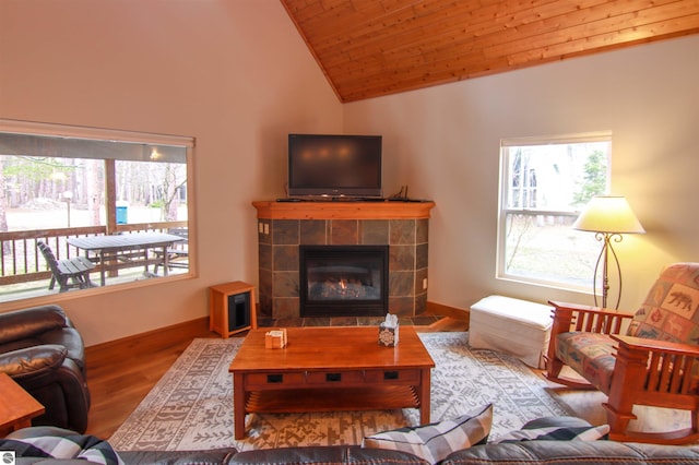 living room with vaulted ceiling, a tile fireplace, baseboards, and wood finished floors
