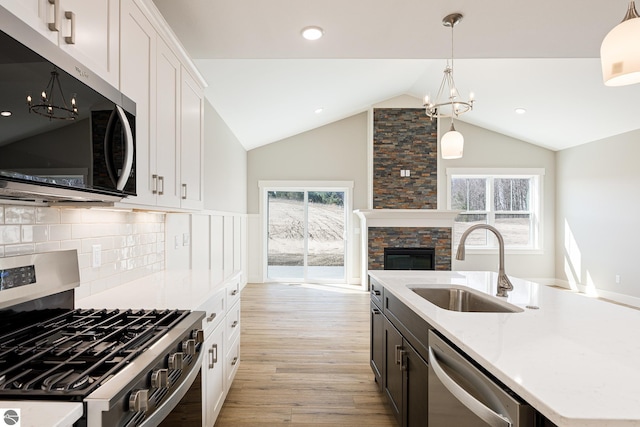 kitchen with lofted ceiling, light wood finished floors, stainless steel appliances, a sink, and a chandelier