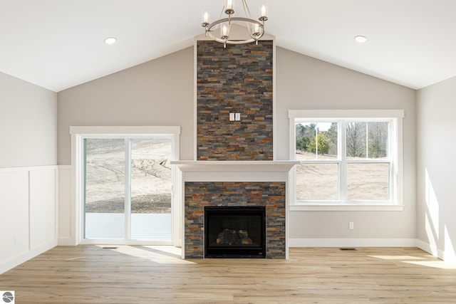 unfurnished living room with vaulted ceiling, a stone fireplace, wood finished floors, and an inviting chandelier