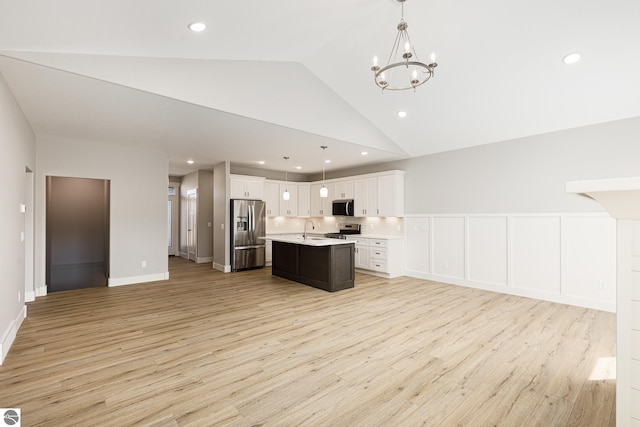 kitchen with a sink, open floor plan, light wood-type flooring, light countertops, and appliances with stainless steel finishes