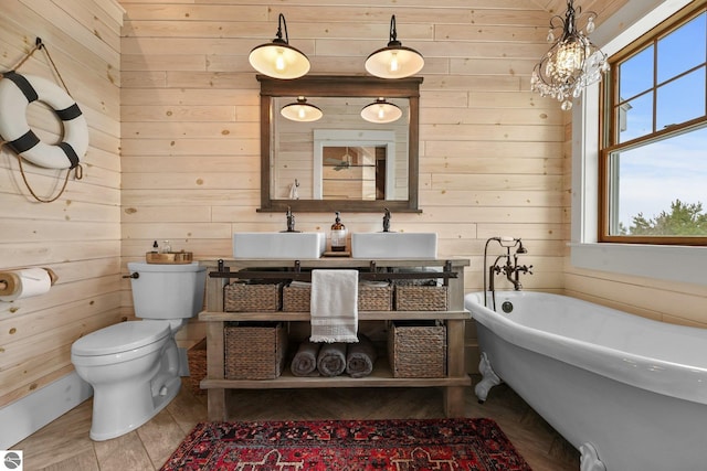full bathroom with toilet, vanity, a chandelier, a soaking tub, and wood walls