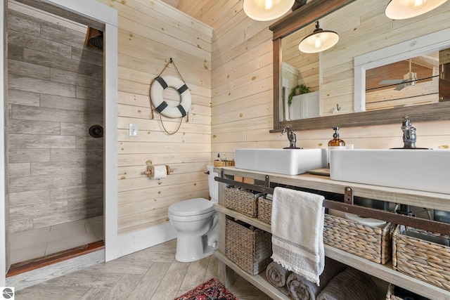 full bath featuring a tile shower, wood walls, toilet, and vanity
