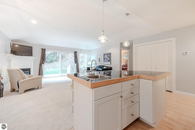 kitchen featuring white cabinets, a sink, a glass covered fireplace, hanging light fixtures, and open floor plan