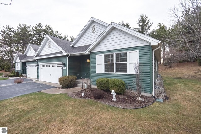 single story home featuring a garage, driveway, a shingled roof, and a front lawn
