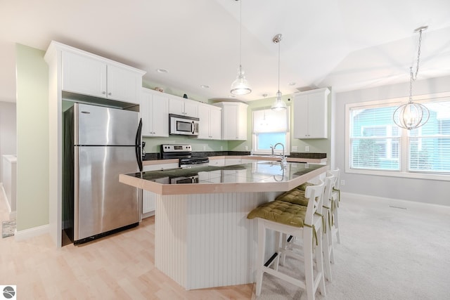 kitchen with white cabinets, baseboards, a center island with sink, appliances with stainless steel finishes, and a breakfast bar area