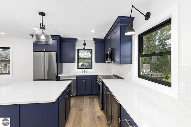 kitchen featuring light wood finished floors, stainless steel appliances, blue cabinets, light stone countertops, and decorative backsplash