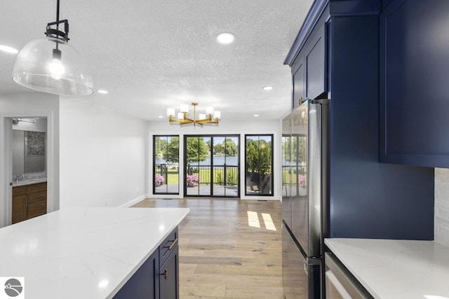 kitchen with blue cabinets, open floor plan, a textured ceiling, and freestanding refrigerator