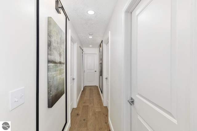 corridor with light wood-style flooring, baseboards, recessed lighting, and a textured ceiling
