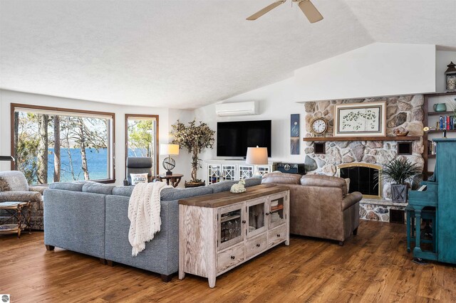living area featuring a wall mounted air conditioner, vaulted ceiling, a stone fireplace, a ceiling fan, and wood finished floors