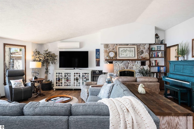 living room with a textured ceiling, vaulted ceiling, a wall mounted air conditioner, wood finished floors, and a stone fireplace