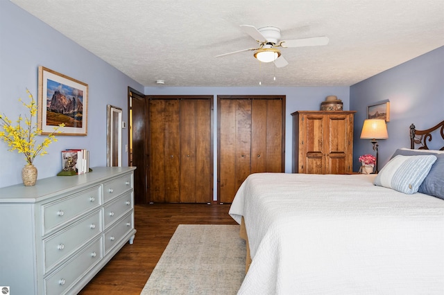 bedroom featuring a ceiling fan, a textured ceiling, two closets, and dark wood-style flooring