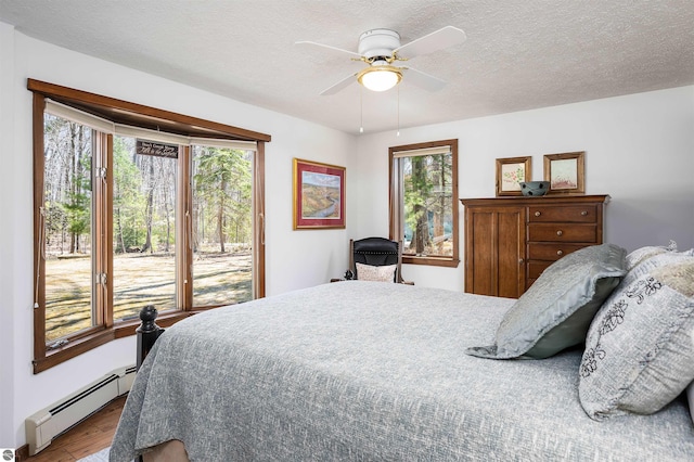 bedroom with multiple windows, wood finished floors, a baseboard radiator, and access to exterior
