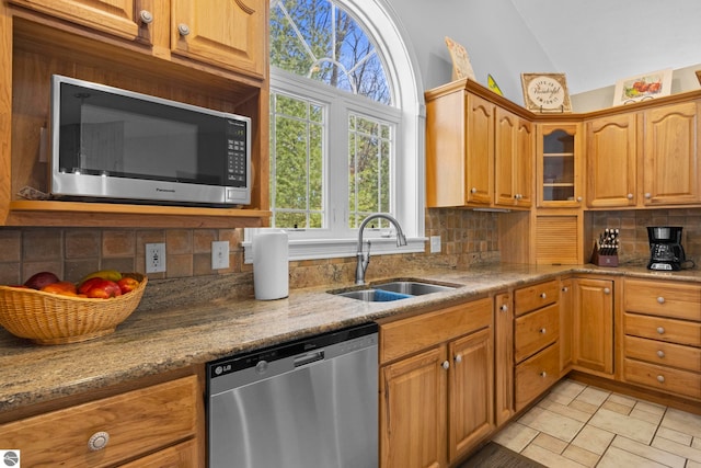 kitchen featuring light stone countertops, glass insert cabinets, tasteful backsplash, a sink, and stainless steel appliances
