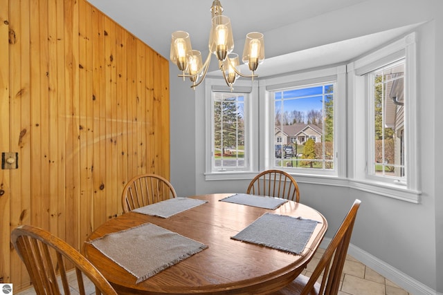 tiled dining room with baseboards, plenty of natural light, wood walls, and a notable chandelier