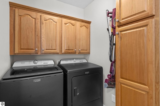 clothes washing area with separate washer and dryer and cabinet space