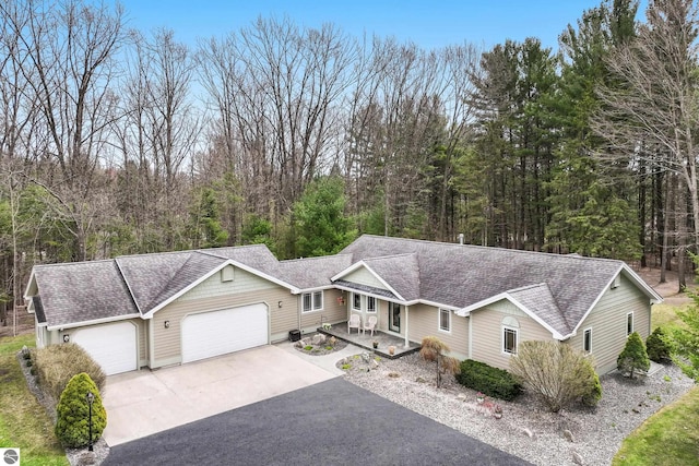 ranch-style house with a view of trees, driveway, roof with shingles, and a garage