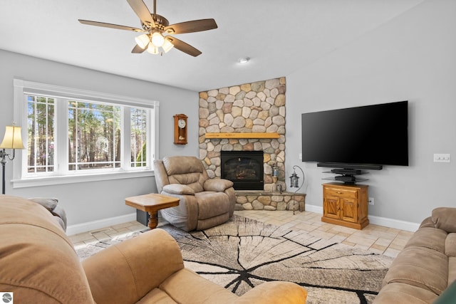 living area with baseboards, a ceiling fan, and a stone fireplace