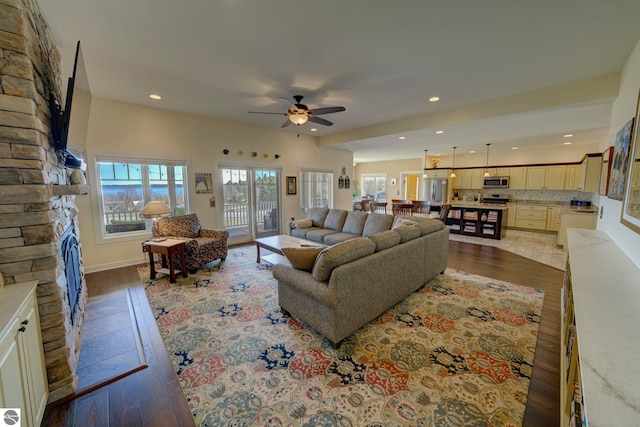 living room with a stone fireplace, wood finished floors, recessed lighting, and ceiling fan