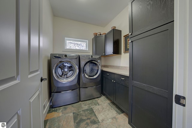 washroom featuring cabinet space, stone finish floor, and washer and clothes dryer