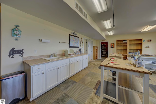 kitchen featuring light countertops, visible vents, light carpet, a sink, and white cabinetry