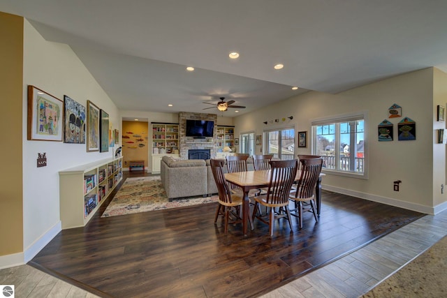 dining room with wood finished floors, baseboards, a ceiling fan, and a stone fireplace