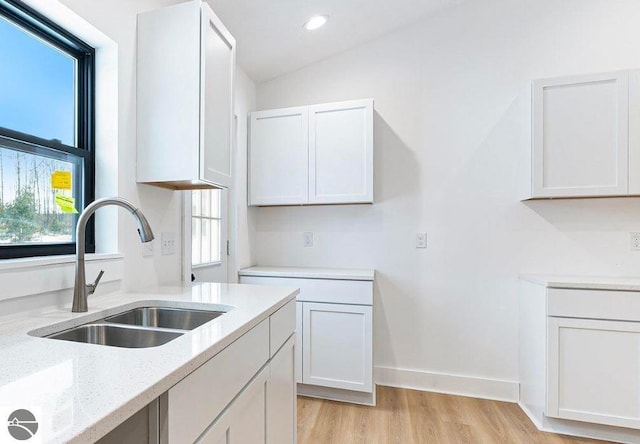 kitchen featuring white cabinets, plenty of natural light, light stone countertops, and a sink