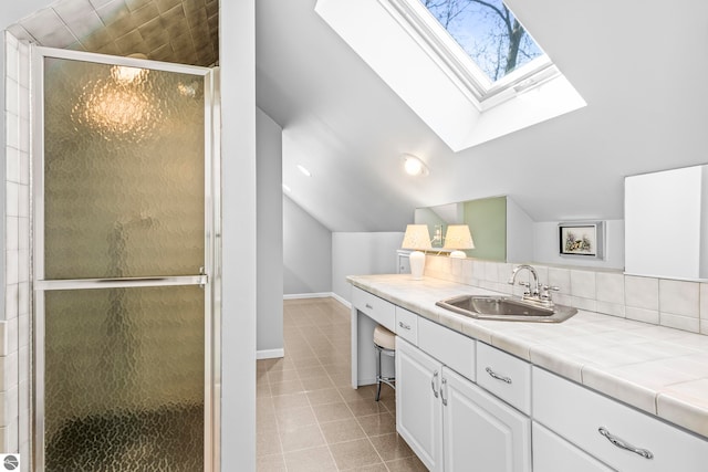 bathroom with lofted ceiling with skylight, a stall shower, vanity, baseboards, and tile patterned flooring