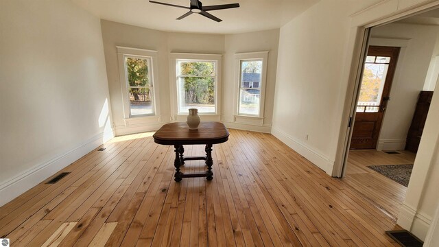 interior space with light wood-type flooring, visible vents, a ceiling fan, and baseboards