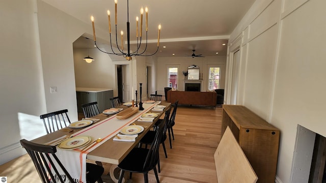 dining room with a fireplace, light wood finished floors, and ceiling fan with notable chandelier